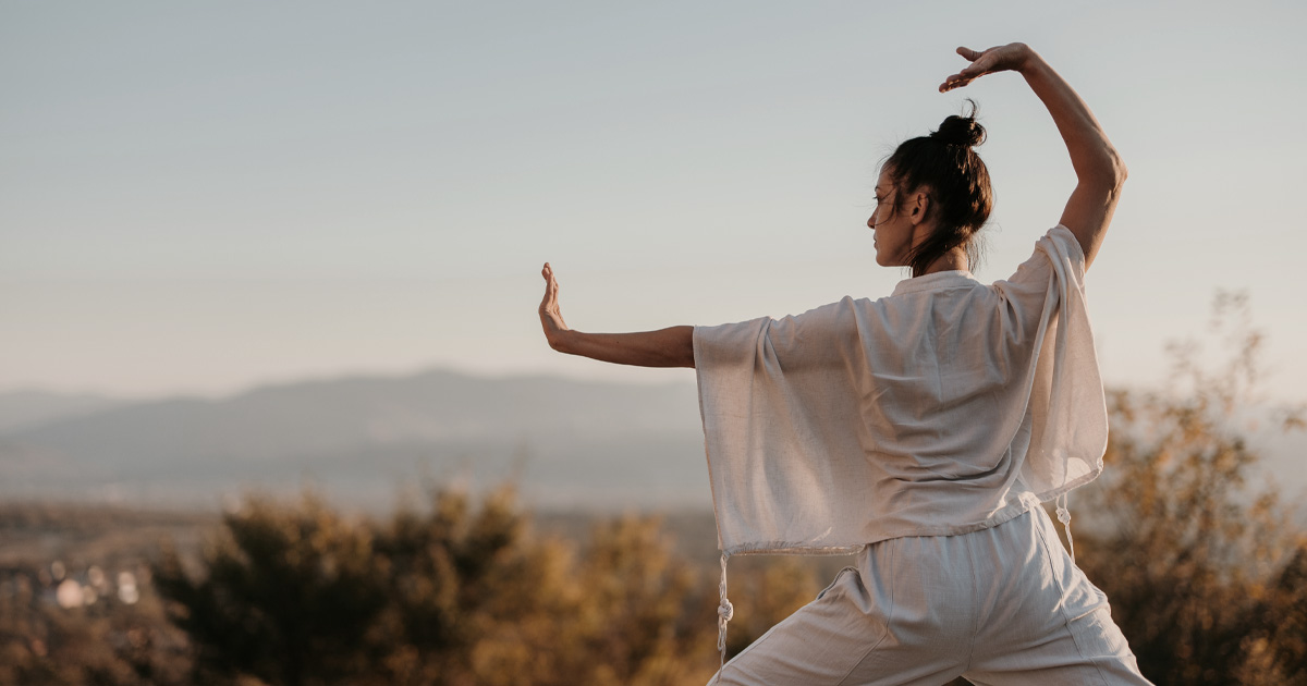 A woman practicing Tai Chi outdoors with mountains in the background.