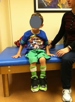 A young boy sitting on a therapy table with both hands on the therapy table surface as an example of a hands-dependent sitter