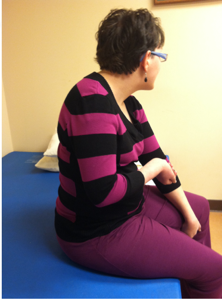 An adult female seated on the edge of a therapy table mat as an example of sitting balance