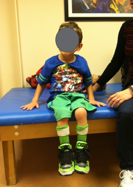 A young boy sitting on a therapy table with both hands on the therapy table surface as an example of a hands-dependent sitter
