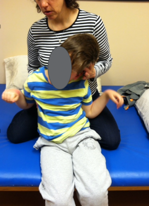 A young boy sitting on a therapy table with both hands raised as an example of a prop sitter