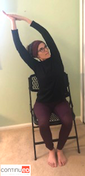 Photo of a young woman sitting in a folding chair and performing the cresent moon yoga pose