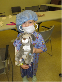 Child in medical garb and a stuffed animal pretending to do medical procedures like practicing with needles